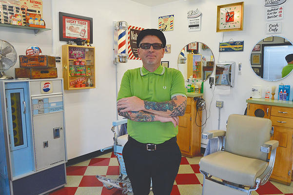 Mac standing with his arms crossed beside the barber chair in his Wardlow Road shop